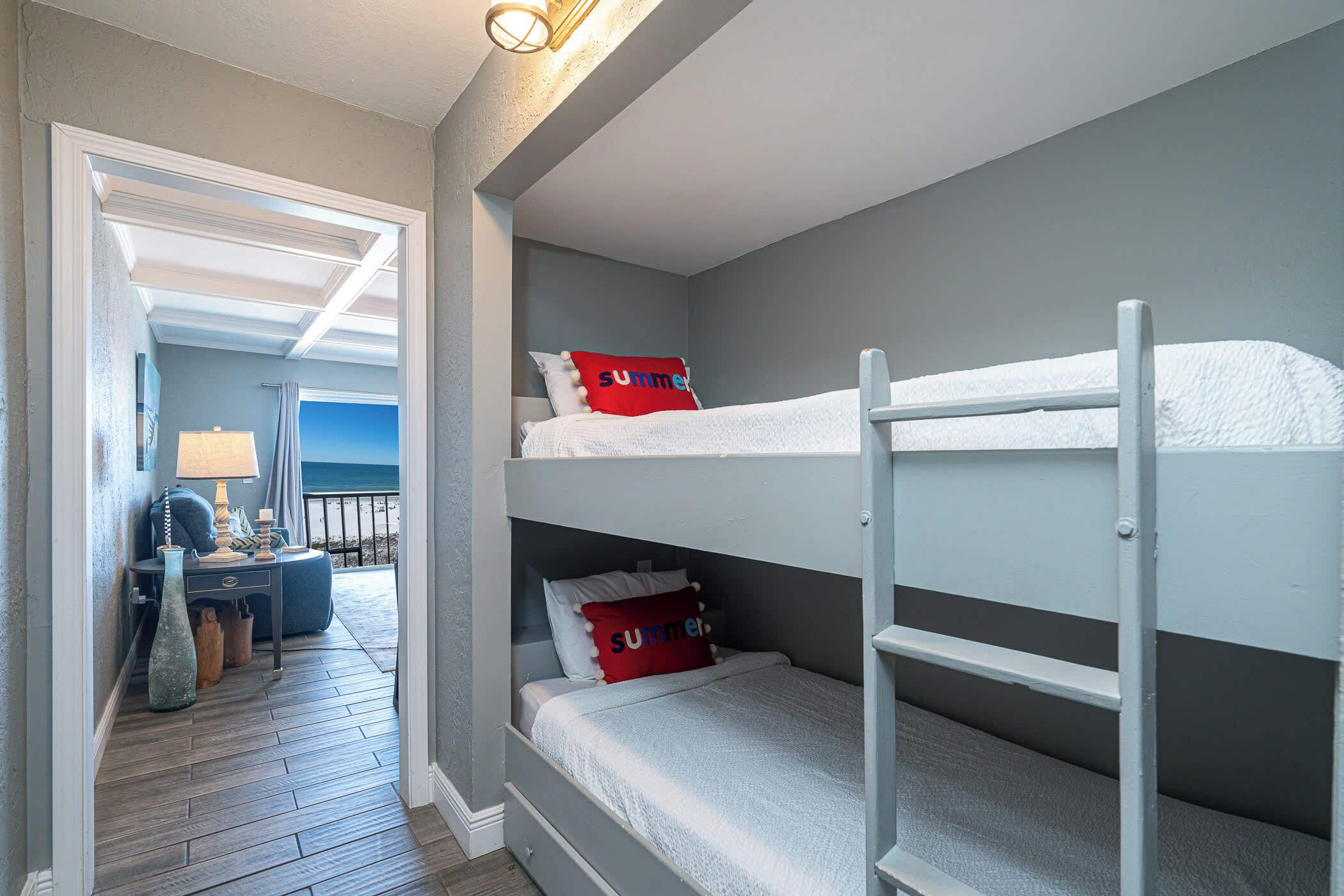 Quarto com beliche, escrivaninha com luminária e vista para o exterior.
