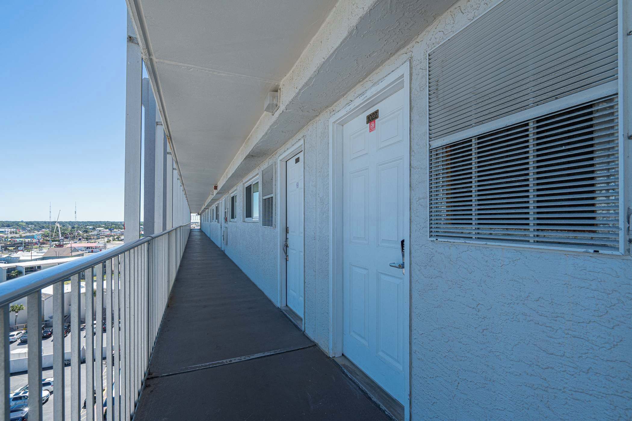 A long, narrow corridor with white doors and windows, leading to a parking area below.