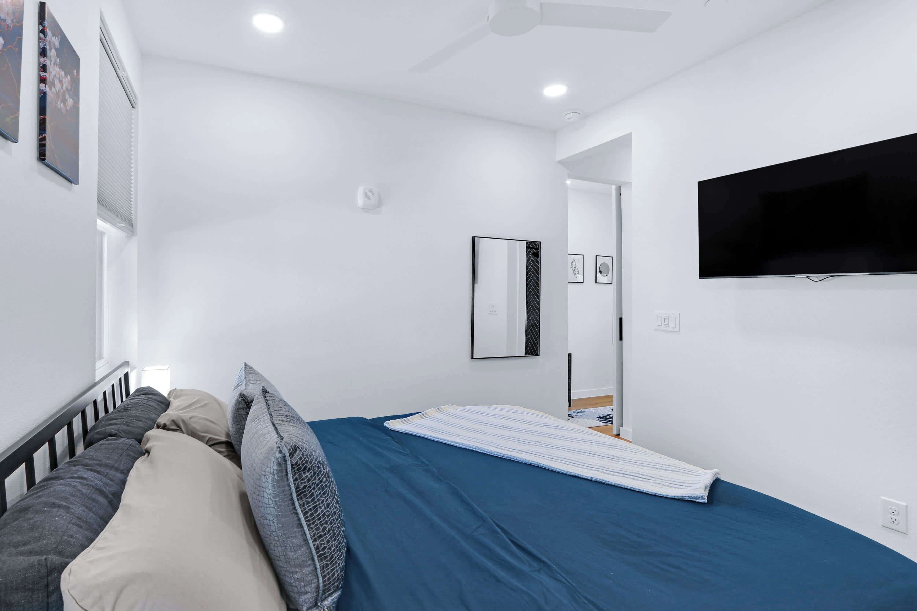 Un dormitorio moderno con cama, almohadas, un televisor de pantalla plana y un ventilador de techo.