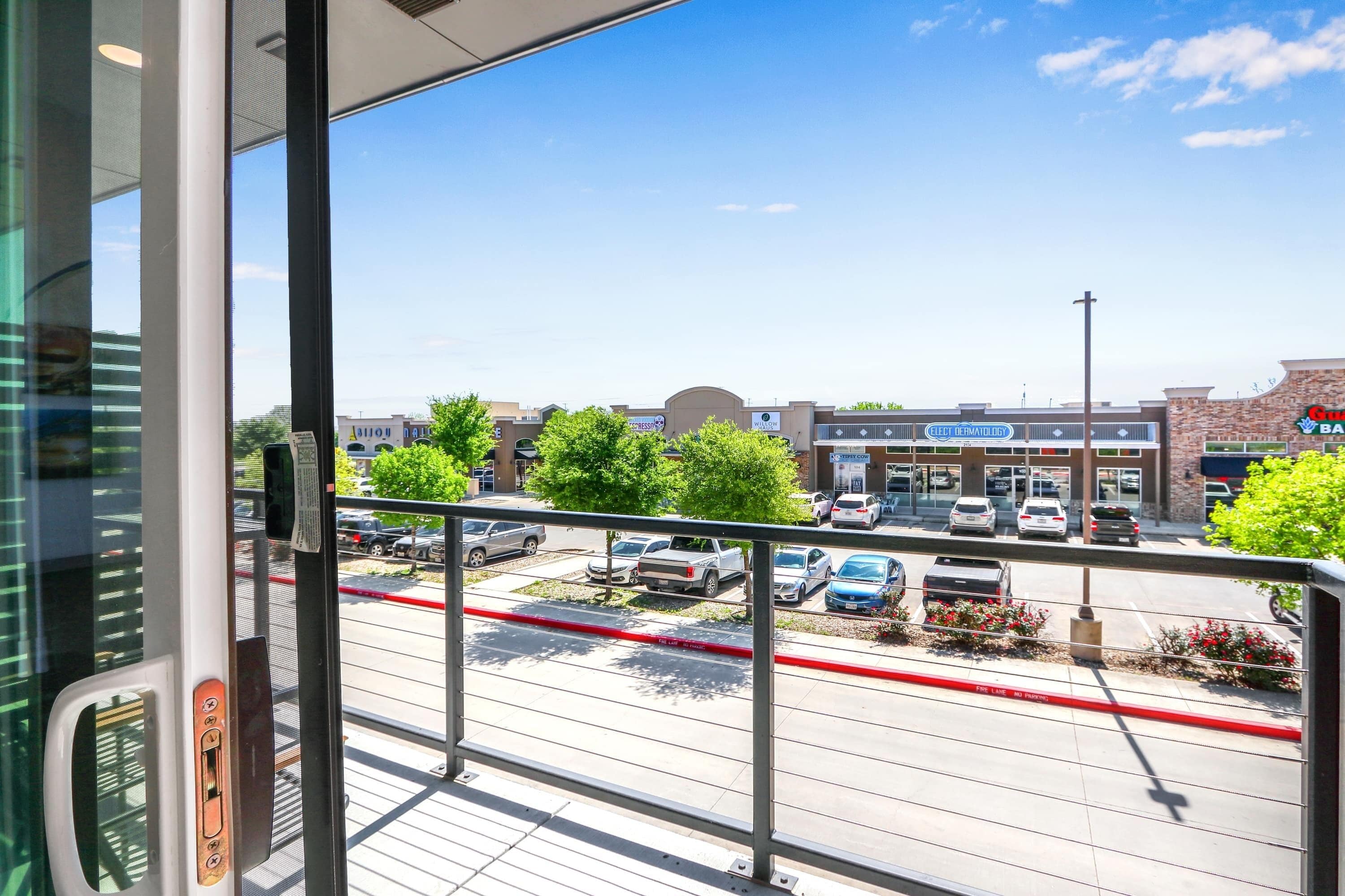 A view from inside a building looking out to a parking lot with several cars and a building with a sign that reads "Grocery & Pharmacy".