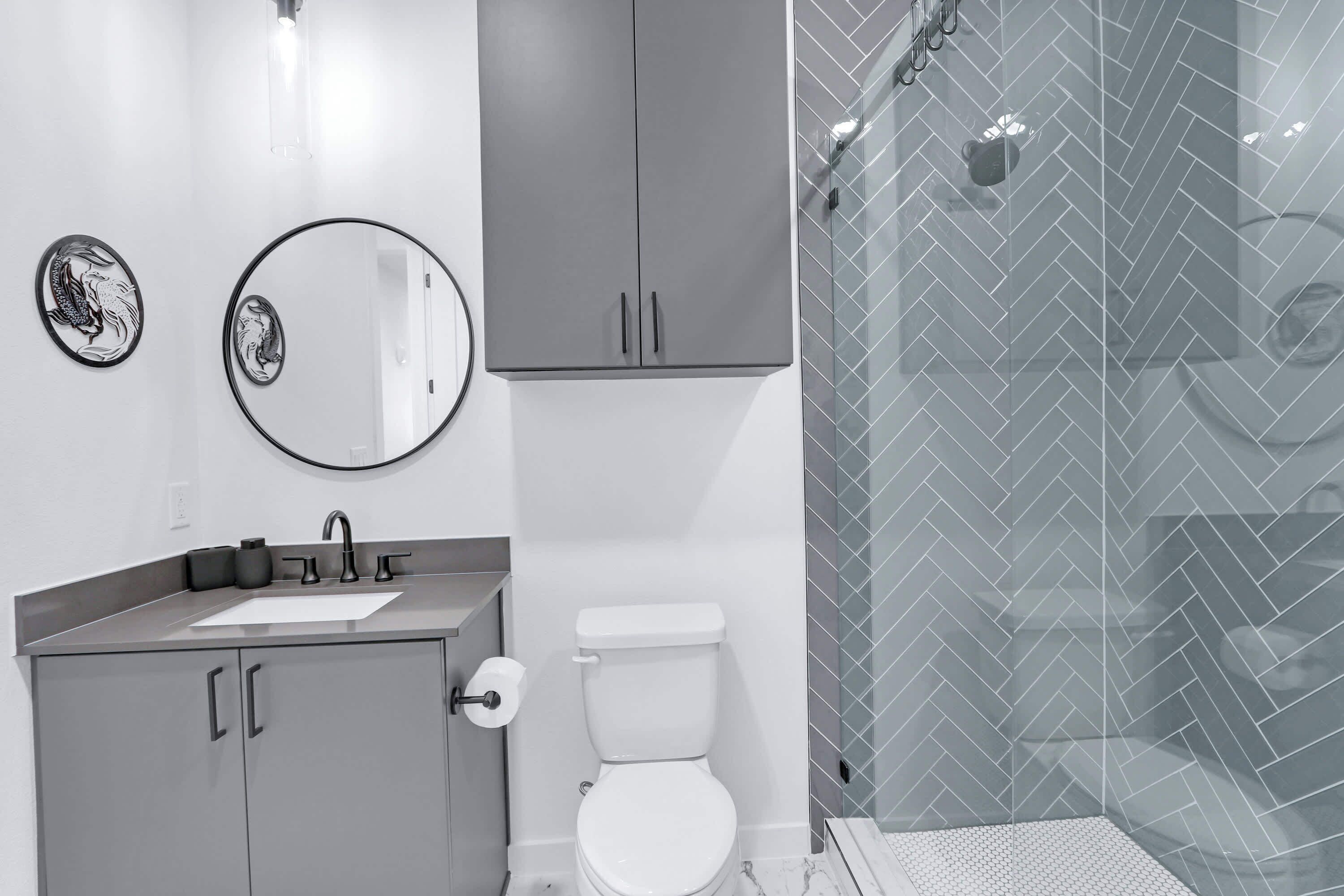 A modern bathroom with a sink, mirror, toilet, and shower area.