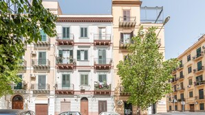 Un immeuble à plusieurs étages, doté de balcons, d’une entrée principale et de voitures garées.