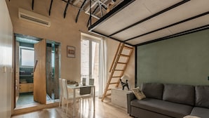 Un salon moderne avec un canapé, une table à manger et des chaises, une échelle et une vue sur l’extérieur.