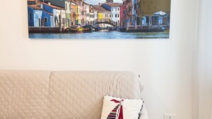 A beige quilted sofa with a single decorative pillow against a wall. - Casa Vacanza Brezza Marina - Marine Pearl (Chioggia)