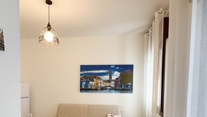 A small, cozy room with a dining table, a sofa, and a painting of a cityscape. - Brezza Marina - Sea Breeze by Ca-sa Check (Chioggia)