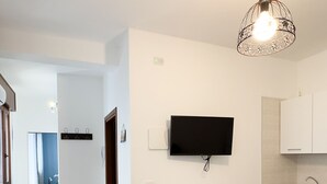 A dining area with a table set for four, a television mounted on the wall, and a kitchen area with cabinets and a sink. - Brezza Marina - Sea Breeze by Ca-sa Check (Chioggia)
