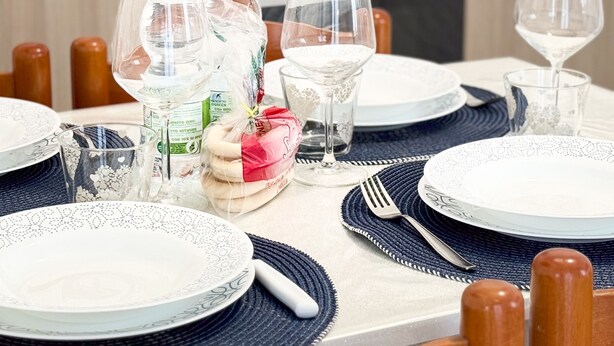 A dining table set with plates, glasses, and cutlery, with a kitchen in the background. - Brezza Marina - Sea Breeze by Ca-sa Check (Chioggia)