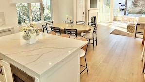 A modern kitchen with a marble island, dining area with chairs, and large windows. - Beach Paradise Stunning 3-story in Long Beach! (Long Beach)