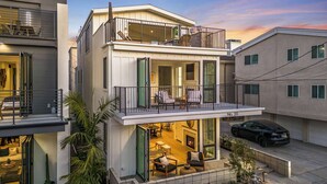Un immeuble résidentiel moderne à deux étages, doté d’un balcon, d’une cheminée et d’une voiture garée dans l’allée.