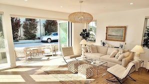 A spacious living room with a sofa, armchairs, and a coffee table, featuring a large window and a hanging light fixture. - Beach Paradise Stunning 3-story in Long Beach! (Long Beach)