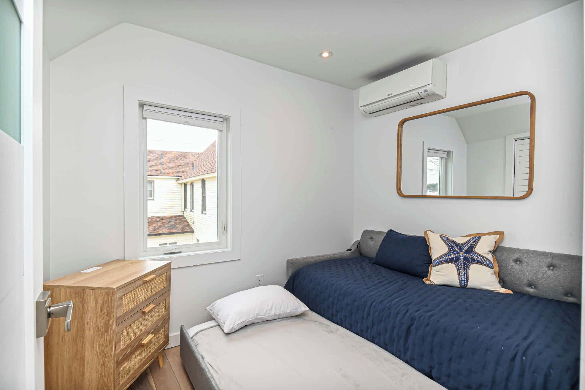 Une chambre à coucher comprenant un lit, une commode, une fenêtre et un appareil de climatisation.