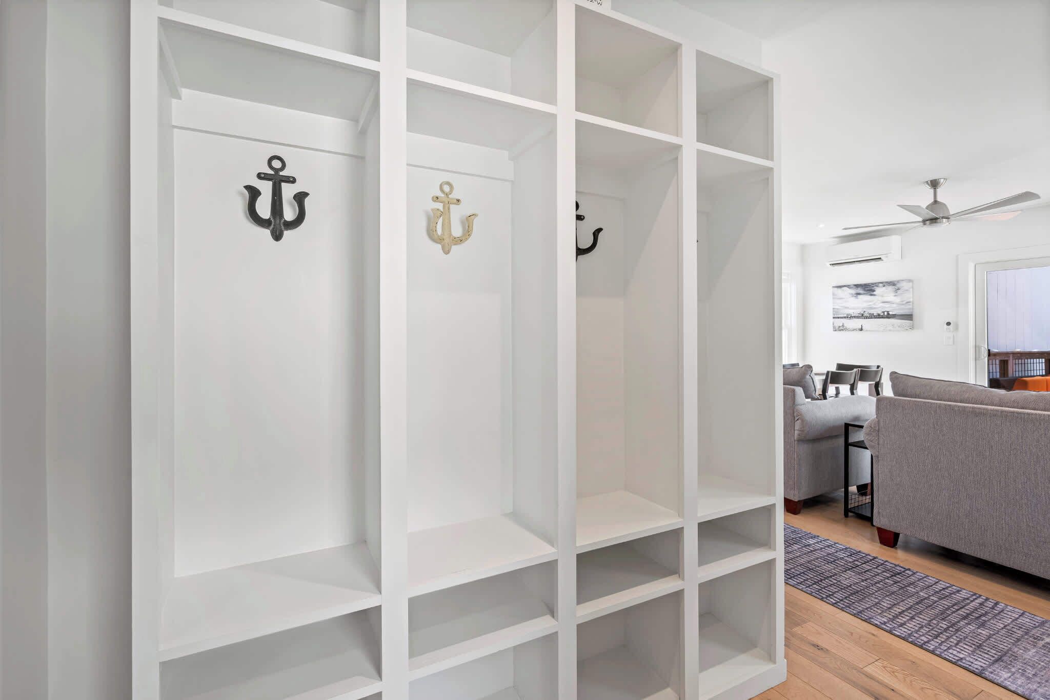 A modern living room with a grey sofa, a ceiling fan, and a white shelving unit with anchor decorations.