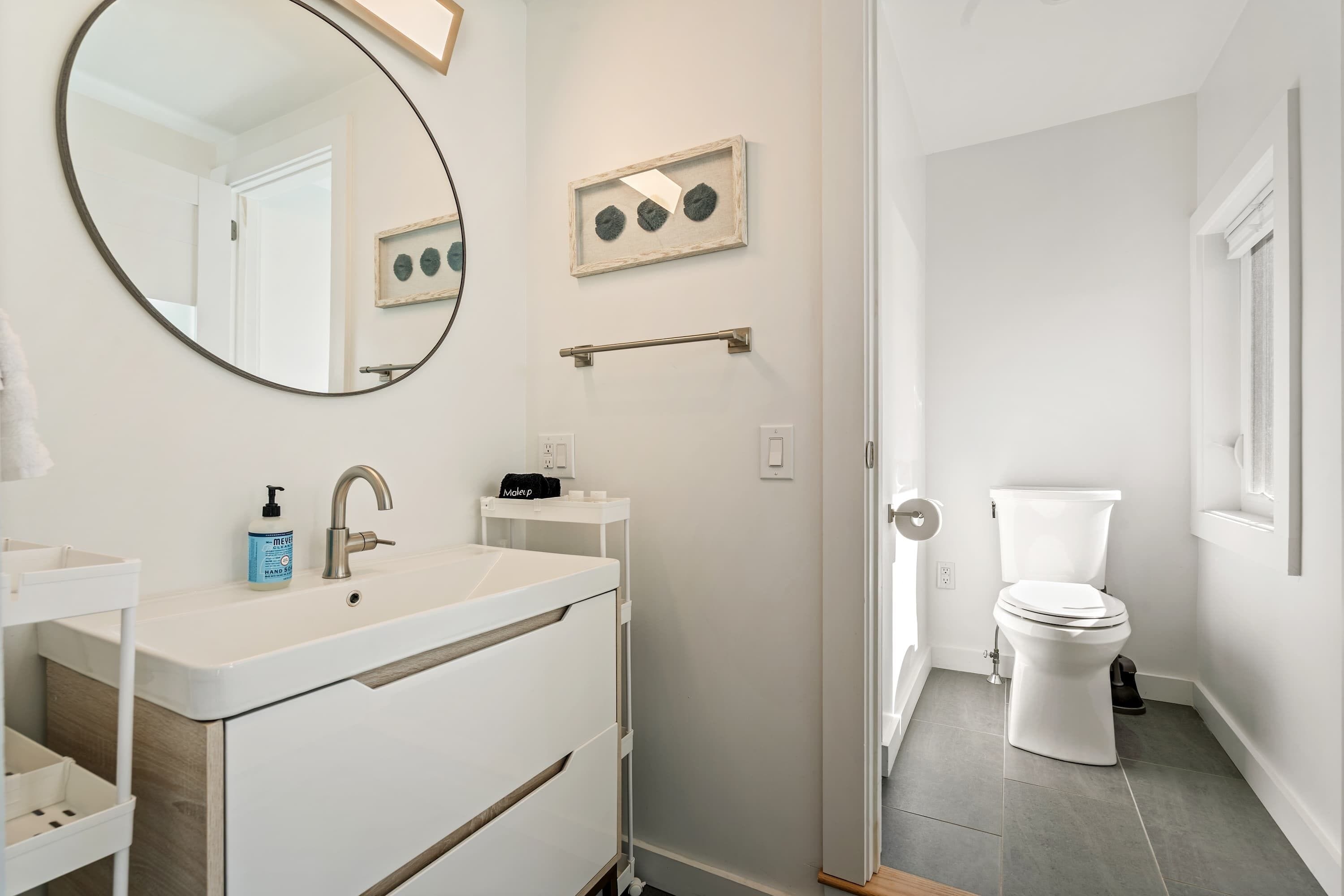A modern bathroom with a white sink, a mirror, a framed artwork, a towel rack, and a toilet.