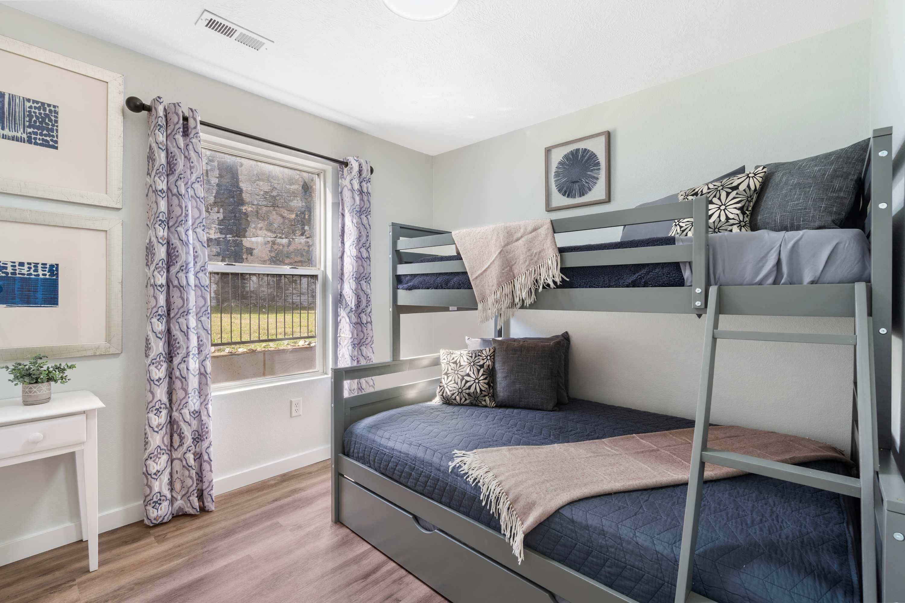 A bunk bed room with a window, a desk, and a potted plant.