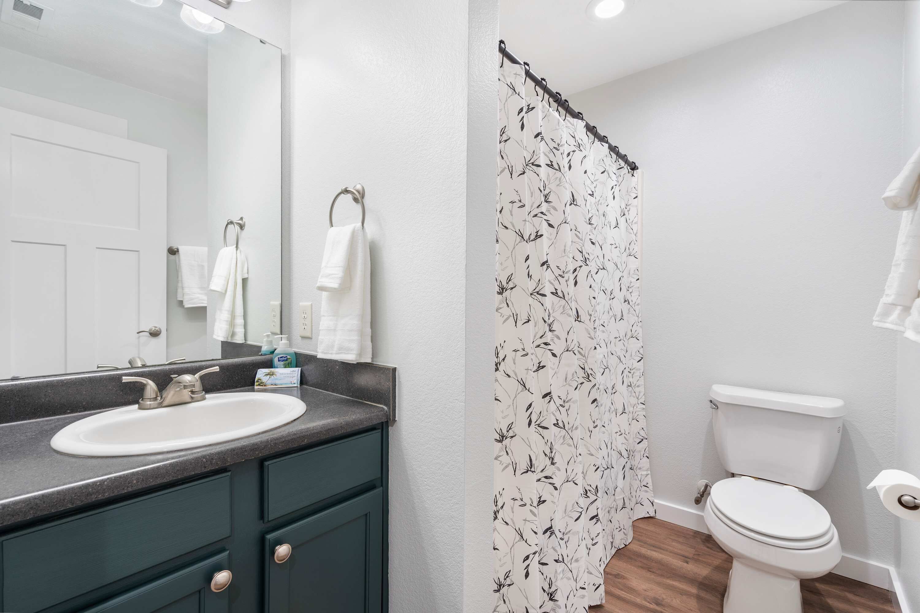 A bathroom with a white sink, dark green cabinets, a white toilet, and a shower curtain with a black leaf pattern.
