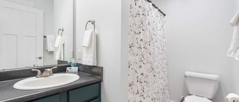 A bathroom with a white sink, dark green cabinets, a white toilet, and a shower curtain with a black leaf pattern.