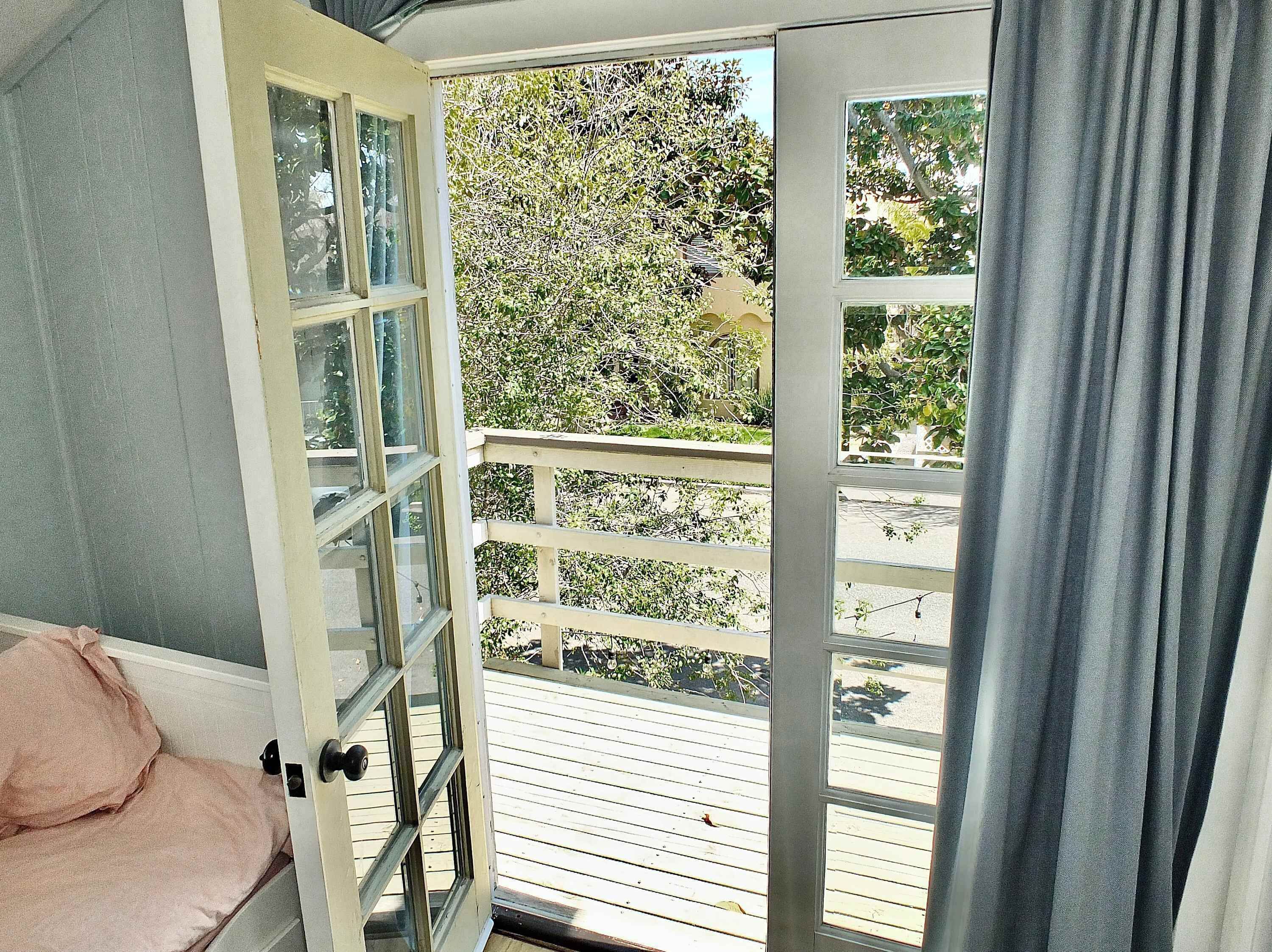 A room with a sliding glass door leading to a balcony with a wooden floor and a view of trees.