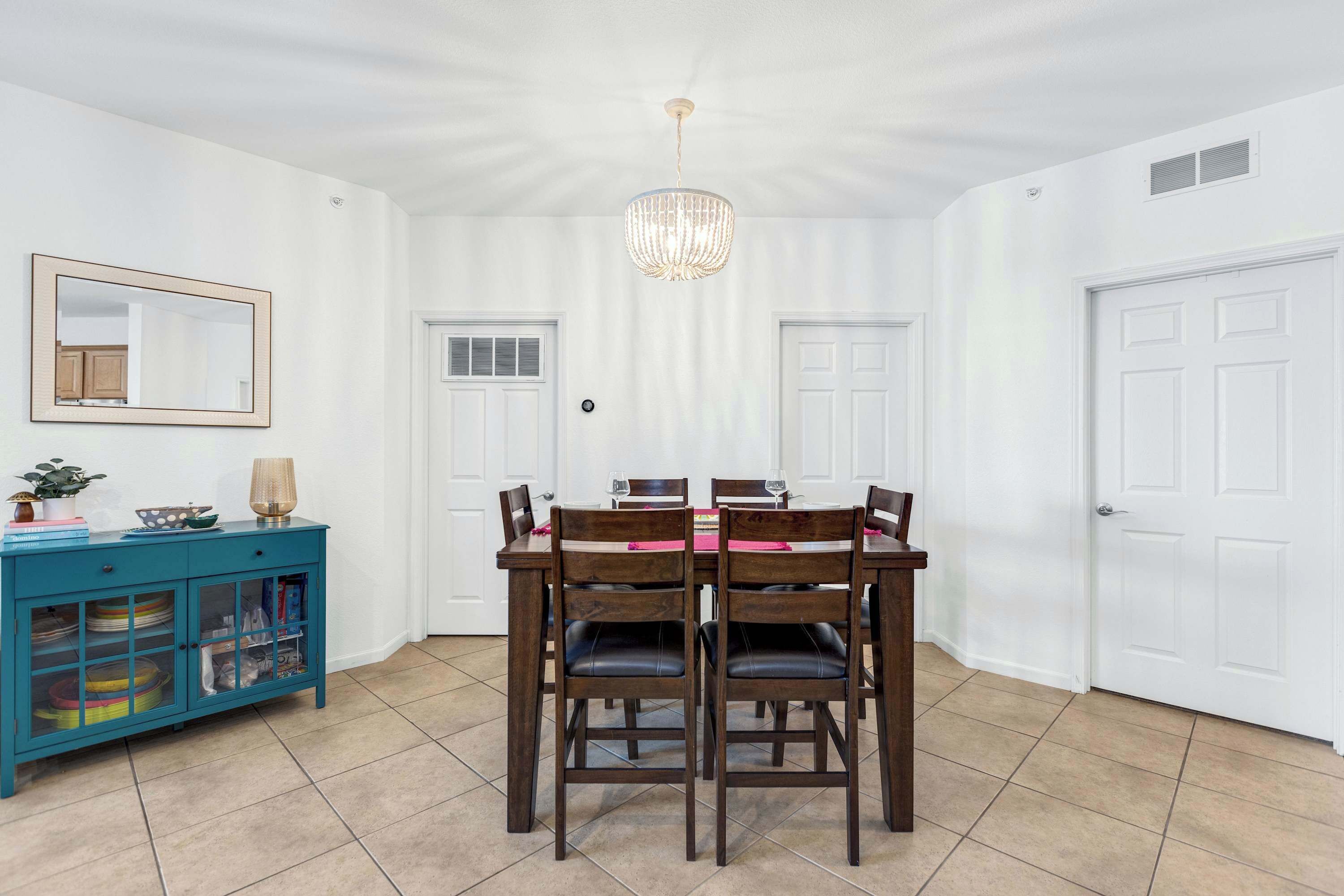 A dining area with a wooden table and chairs, a teal cabinet with glass doors, and a chandelier.