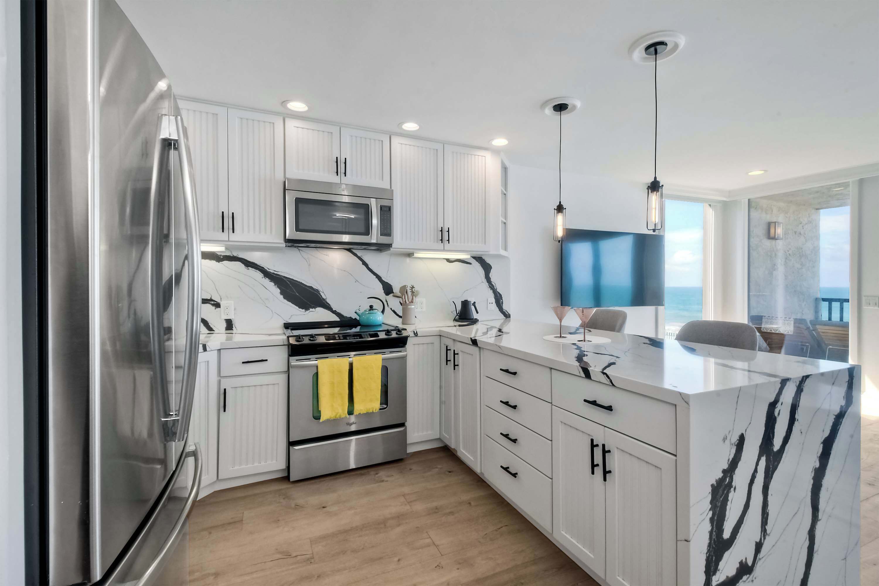 A modern kitchen with white cabinets, stainless steel appliances, and a marble countertop.