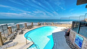 Piscina con vista sull'oceano, circondata da lettini e un cartello che indica la presenza di un bagnino.