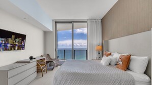 A modern bedroom with a large bed, a desk, and a TV displaying a cityscape. - Luxury Penthouse! 4 BDR With Resort Amenities (Hollywood)