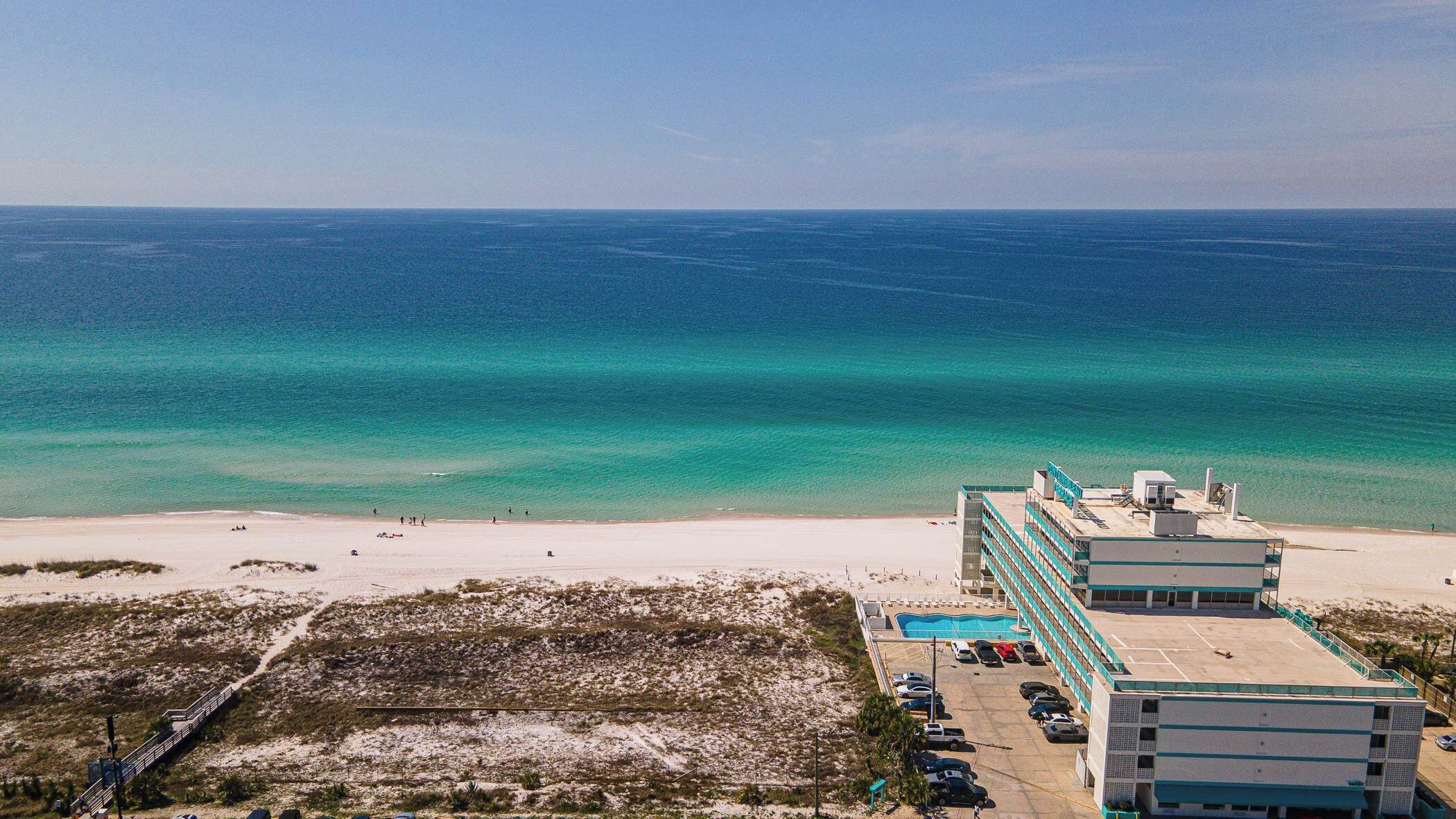 A hotel with a pool, located near a beach with clear blue waters.