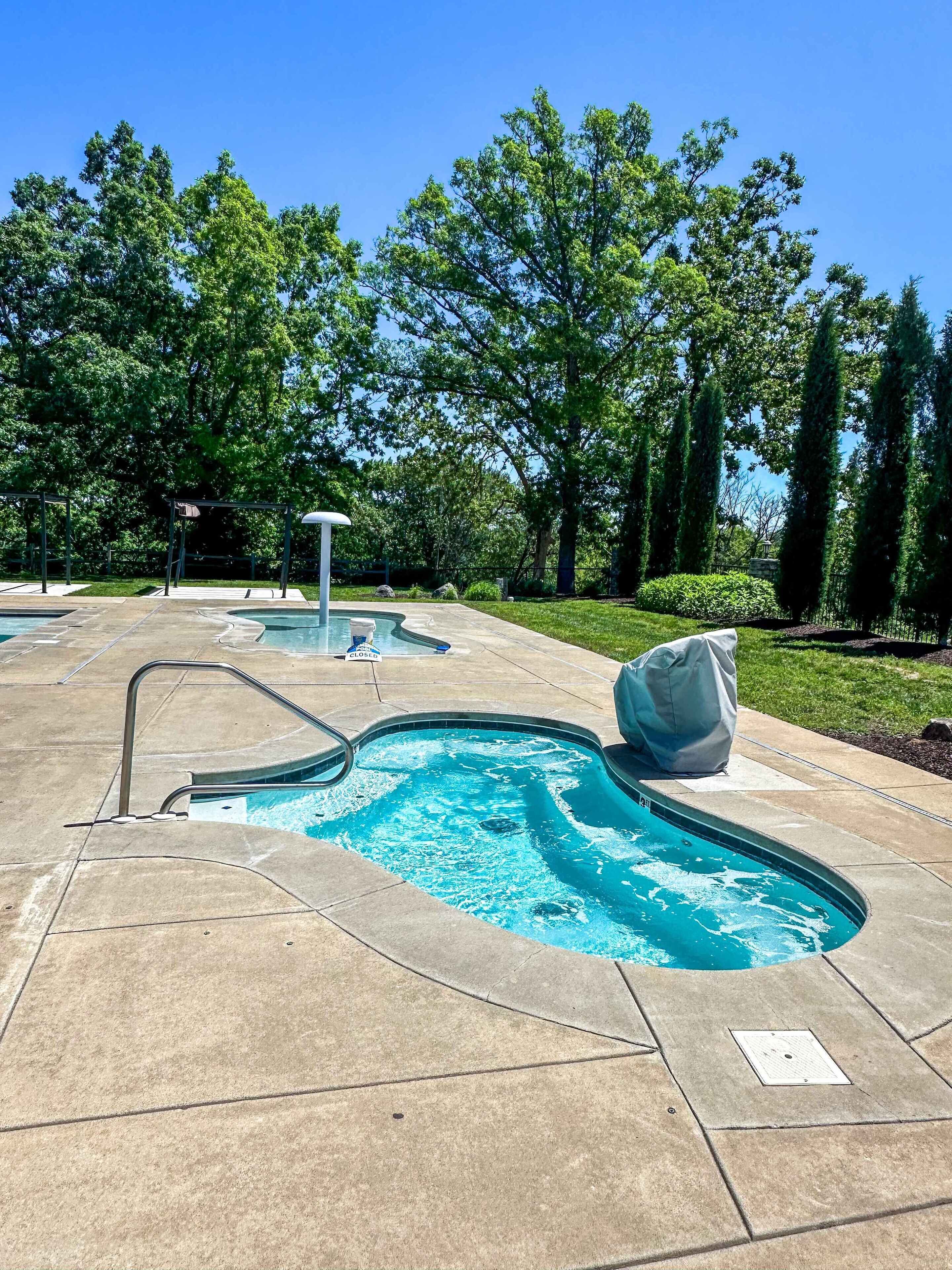 Un área de piscina con varias piscinas, una zona de estar cubierta y abundante vegetación.