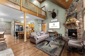 A spacious living area with a stone fireplace, a wooden staircase, and a kitchen in the background. - Royal Moose Lodge A Grand Adventure for 20! (Branson)