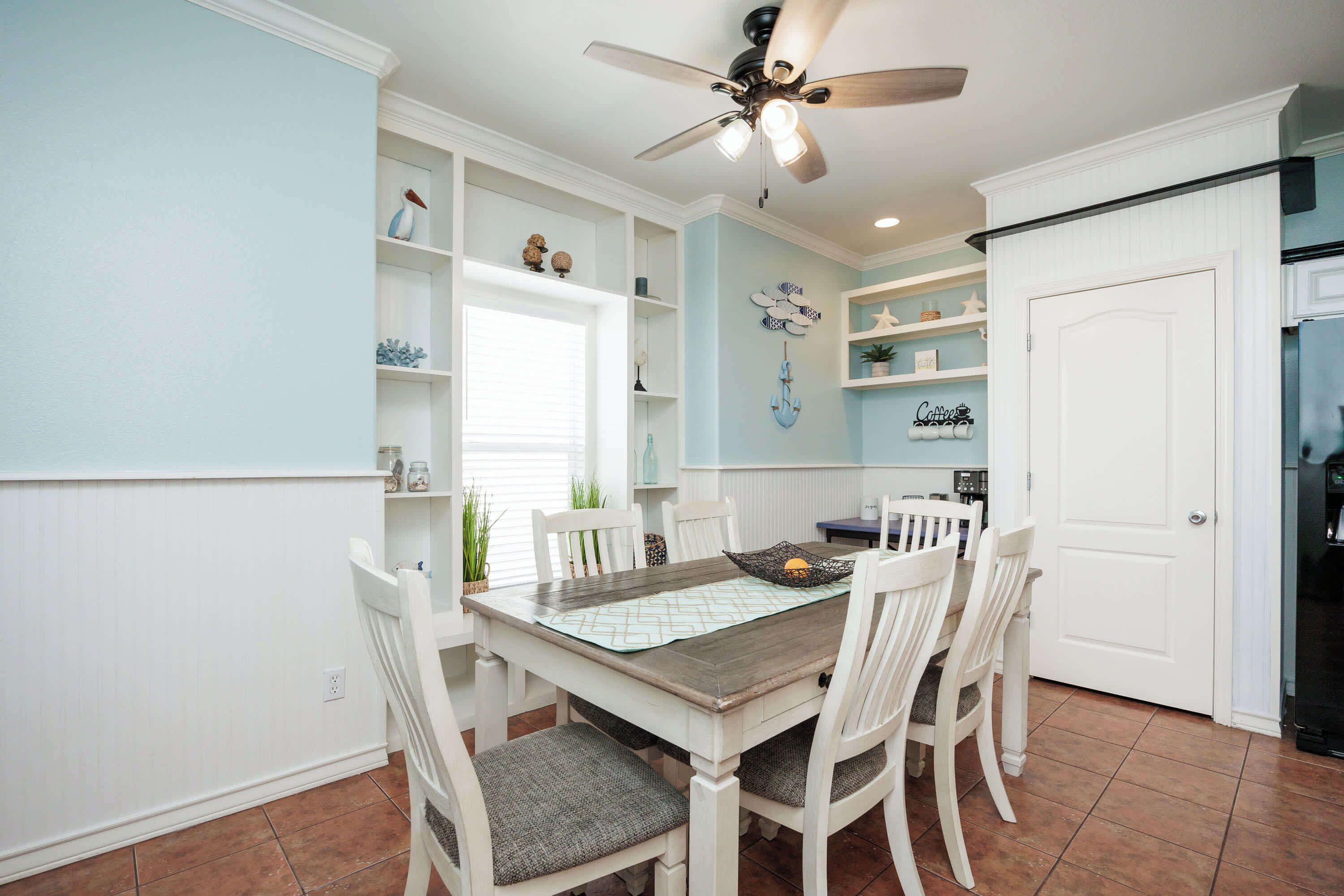 A dining area with a wooden table, white chairs, and a ceiling fan.