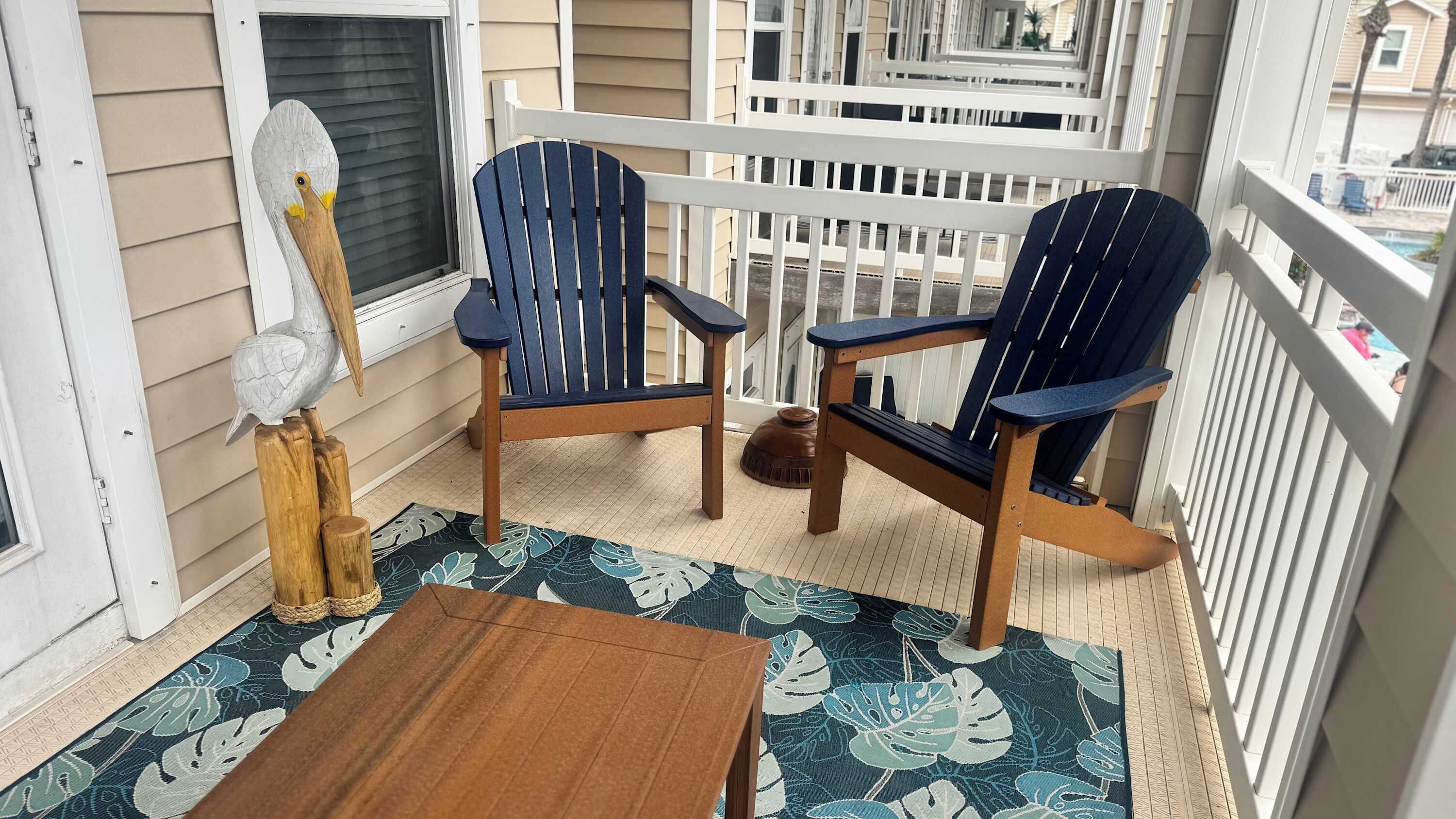 A balcony with two Adirondack chairs, a small table, and a decorative bird sculpture.