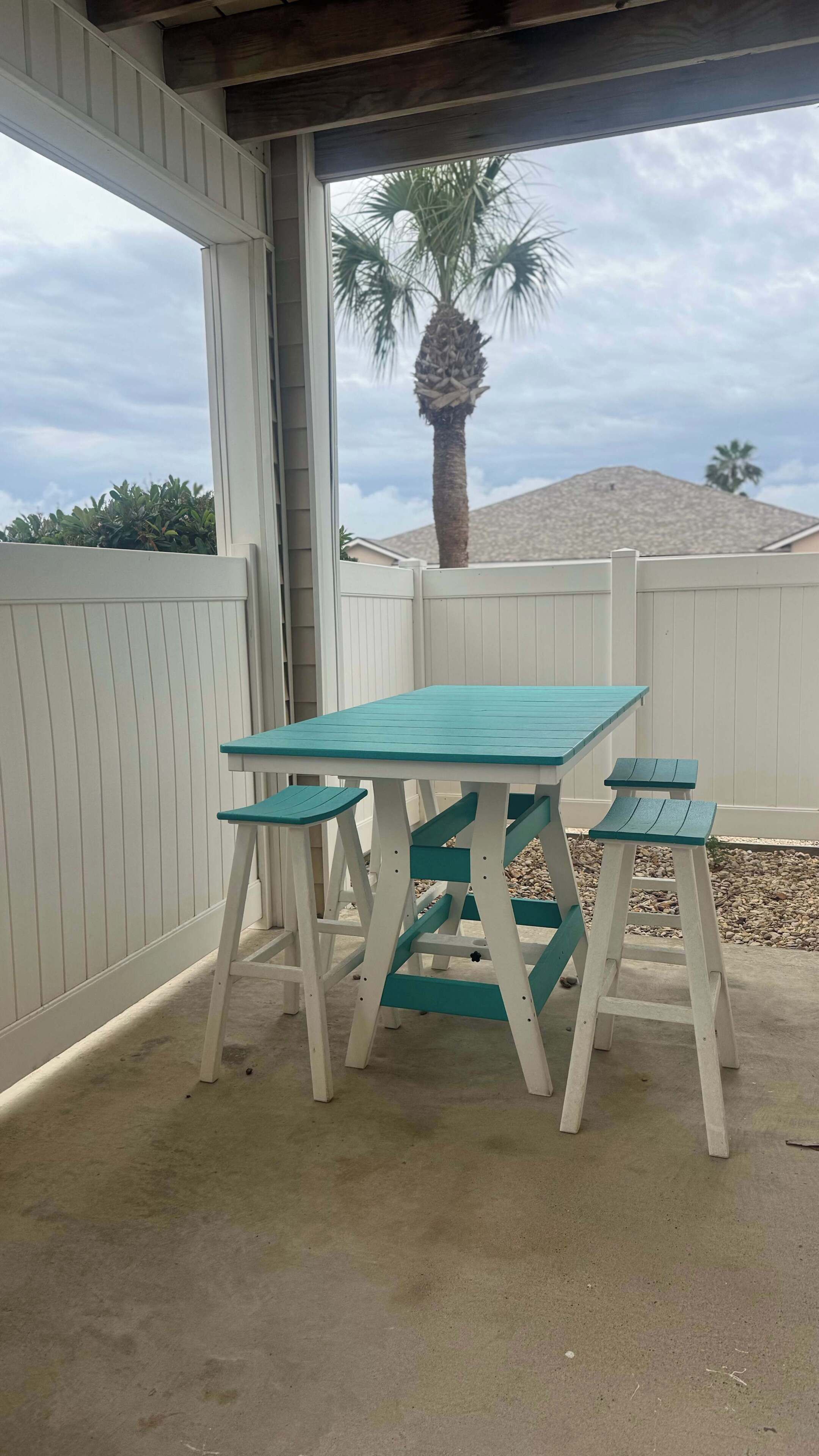 A patio area with a table and benches, a white fence, and a palm tree in the background.