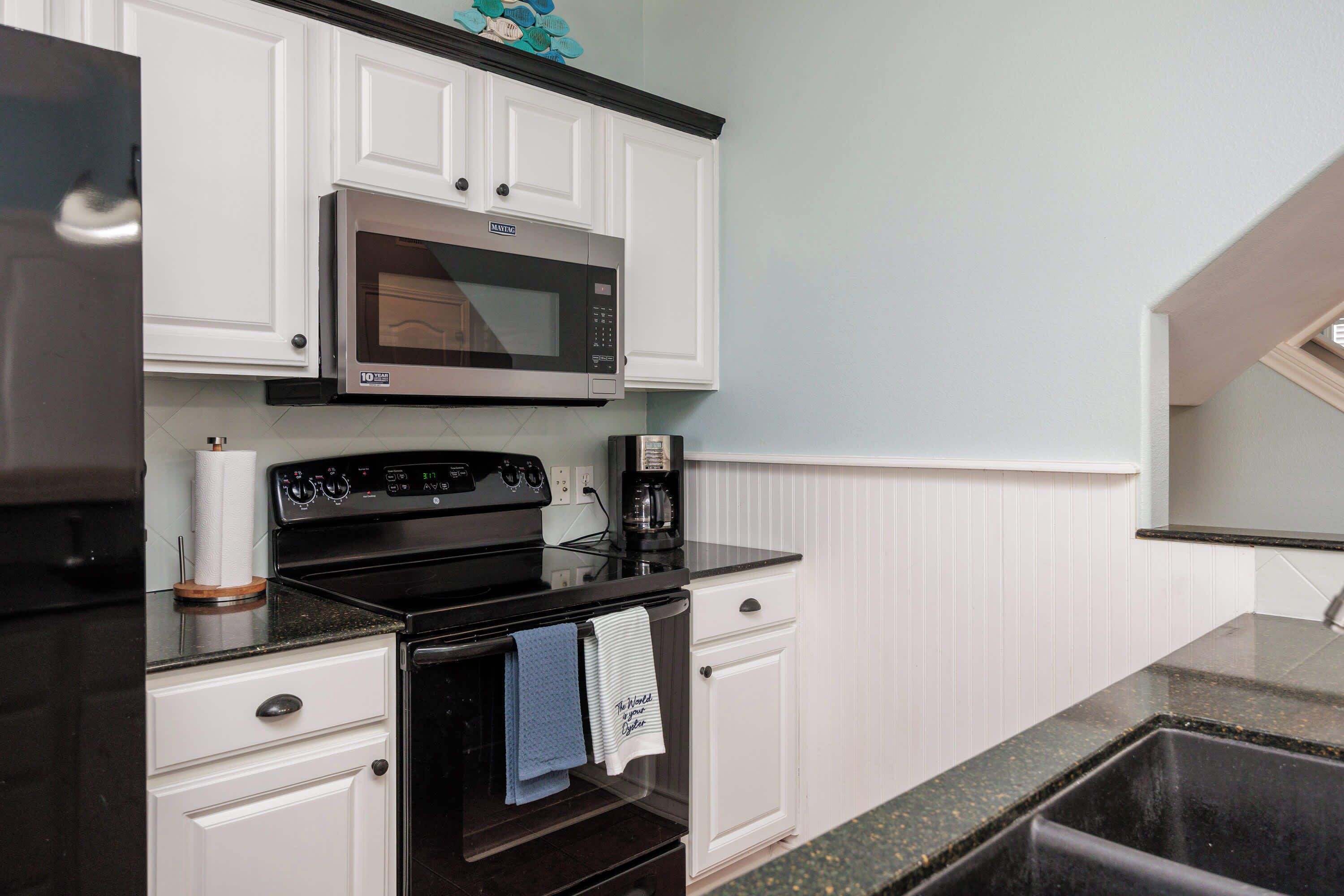 A kitchen with white cabinets, a stainless steel microwave, a black stove, and a sink.