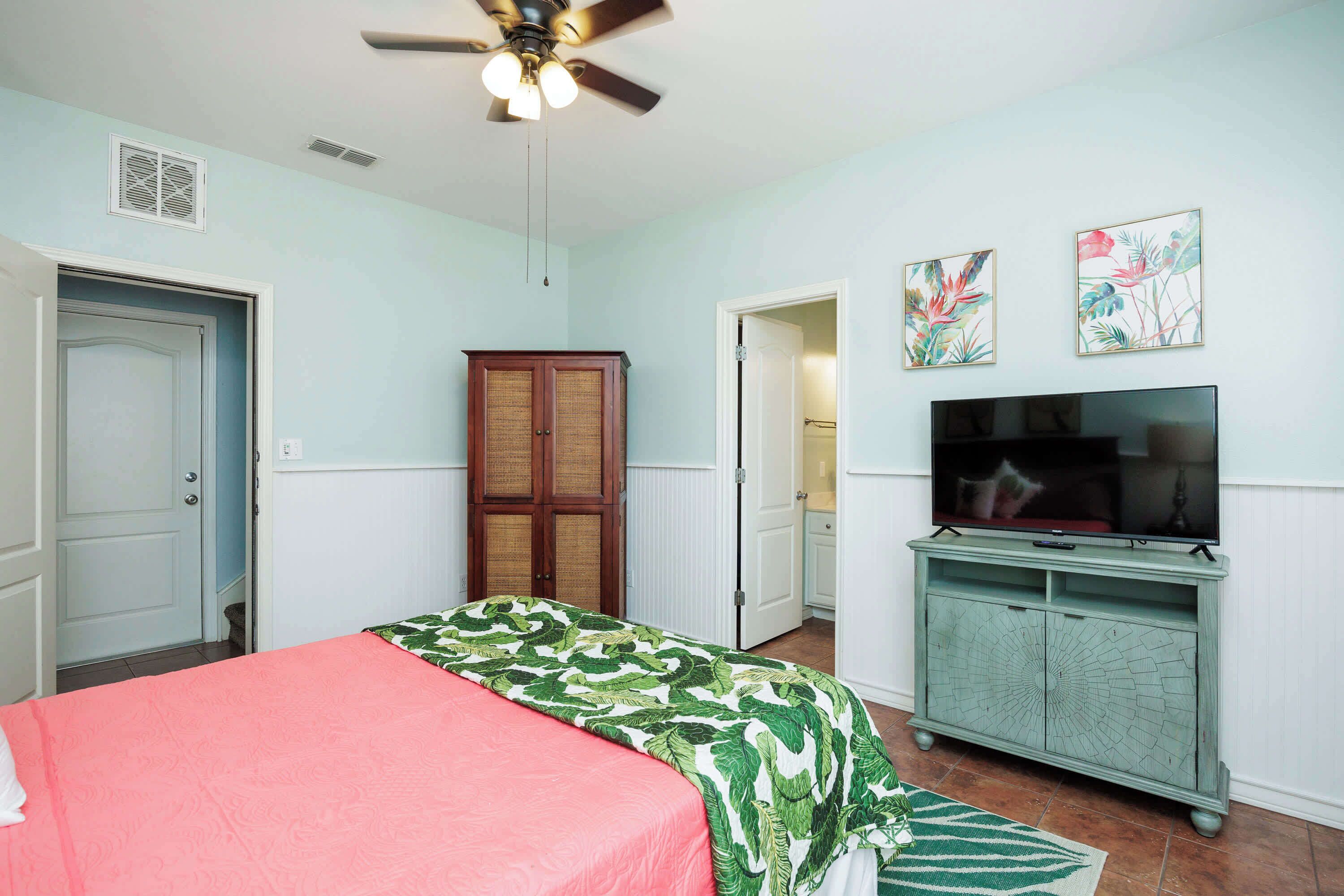 A bedroom with a bed, a television on a cabinet, and a ceiling fan.