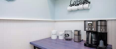 A kitchenette with a coffee station, a sugar container, a coffee mug, a toaster, and a coffee maker.