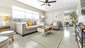 A spacious living room with a grey sofa, a coffee table, and a ceiling fan. There are two chairs, a lamp, and a plant. - Sunny Side Up A Charming Retreat! (Tampa)