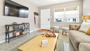 A modern living room with a flat-screen TV, a wooden coffee table, a sofa, and a window with blinds. - Sunny Side Up A Charming Retreat! (Tampa)