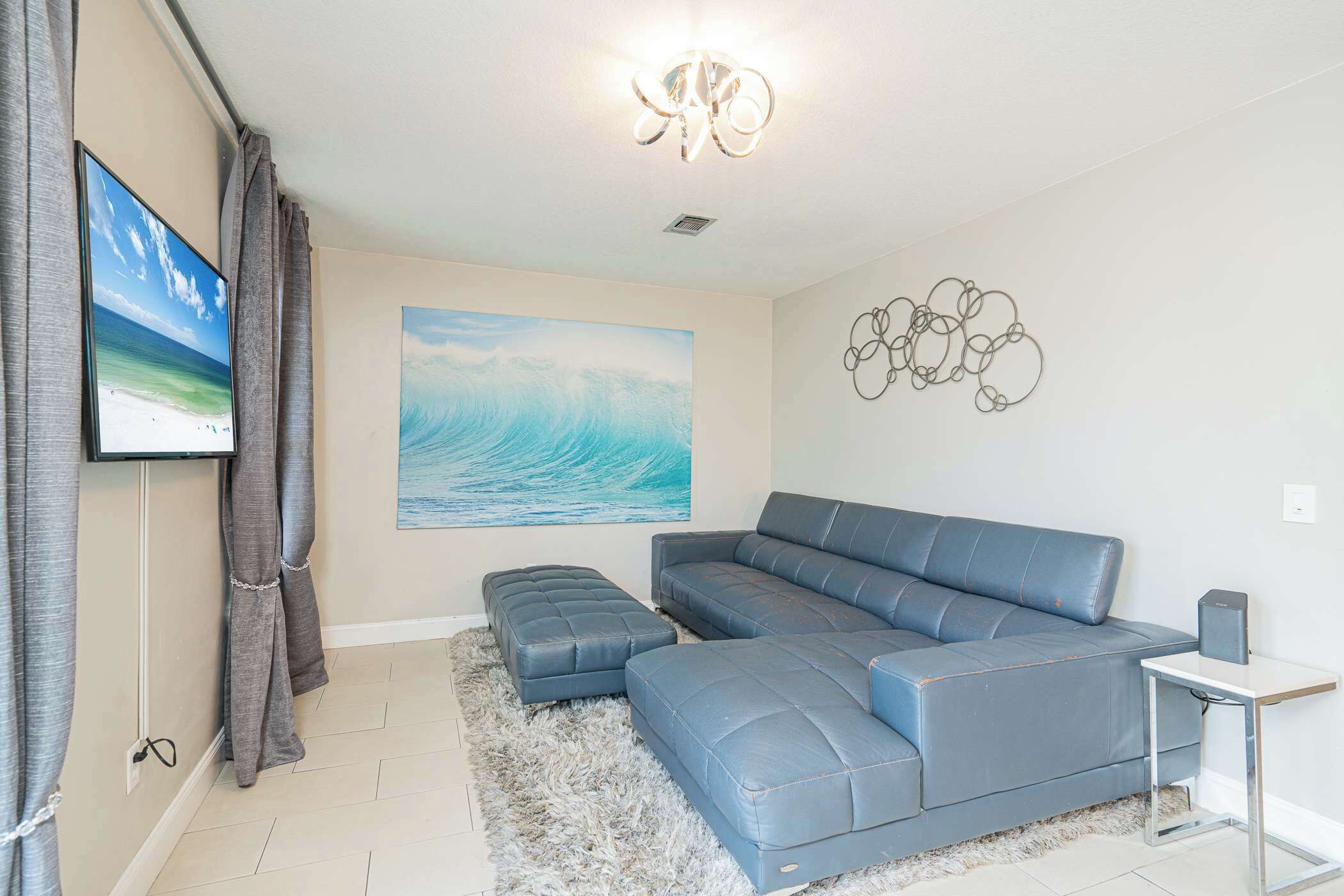 A living room with a sectional sofa, a flat-screen TV, a painting of a wave, and a modern chandelier.