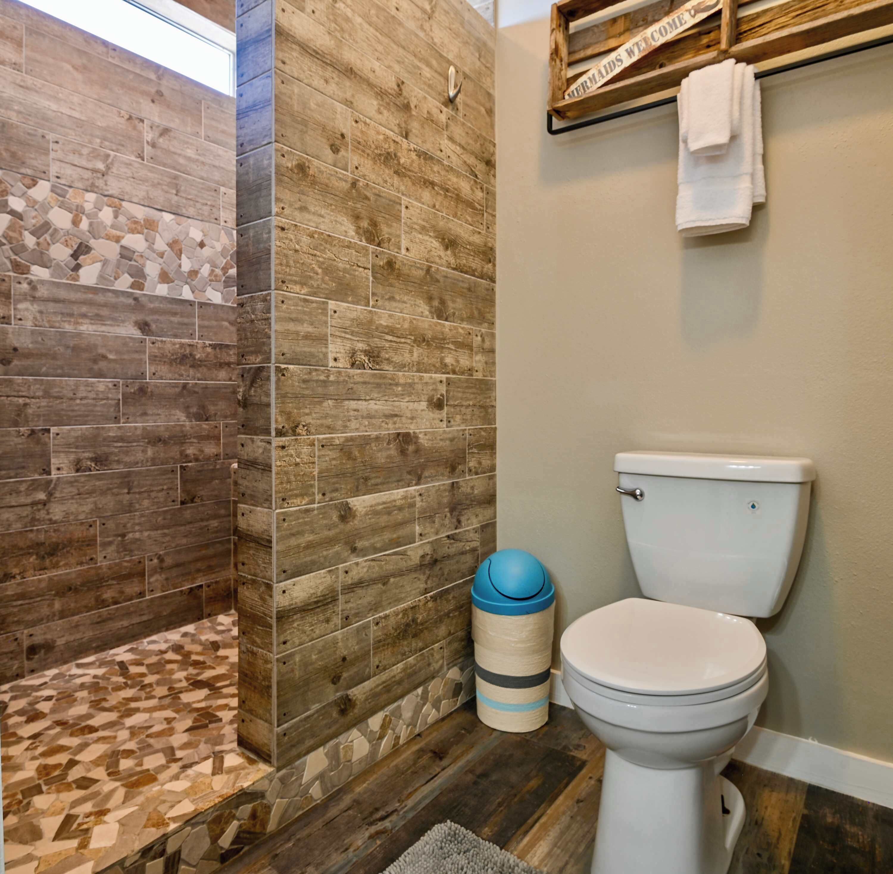 Une salle de bain avec un mur en bois, une zone de douche carrelée, des toilettes et une poubelle.