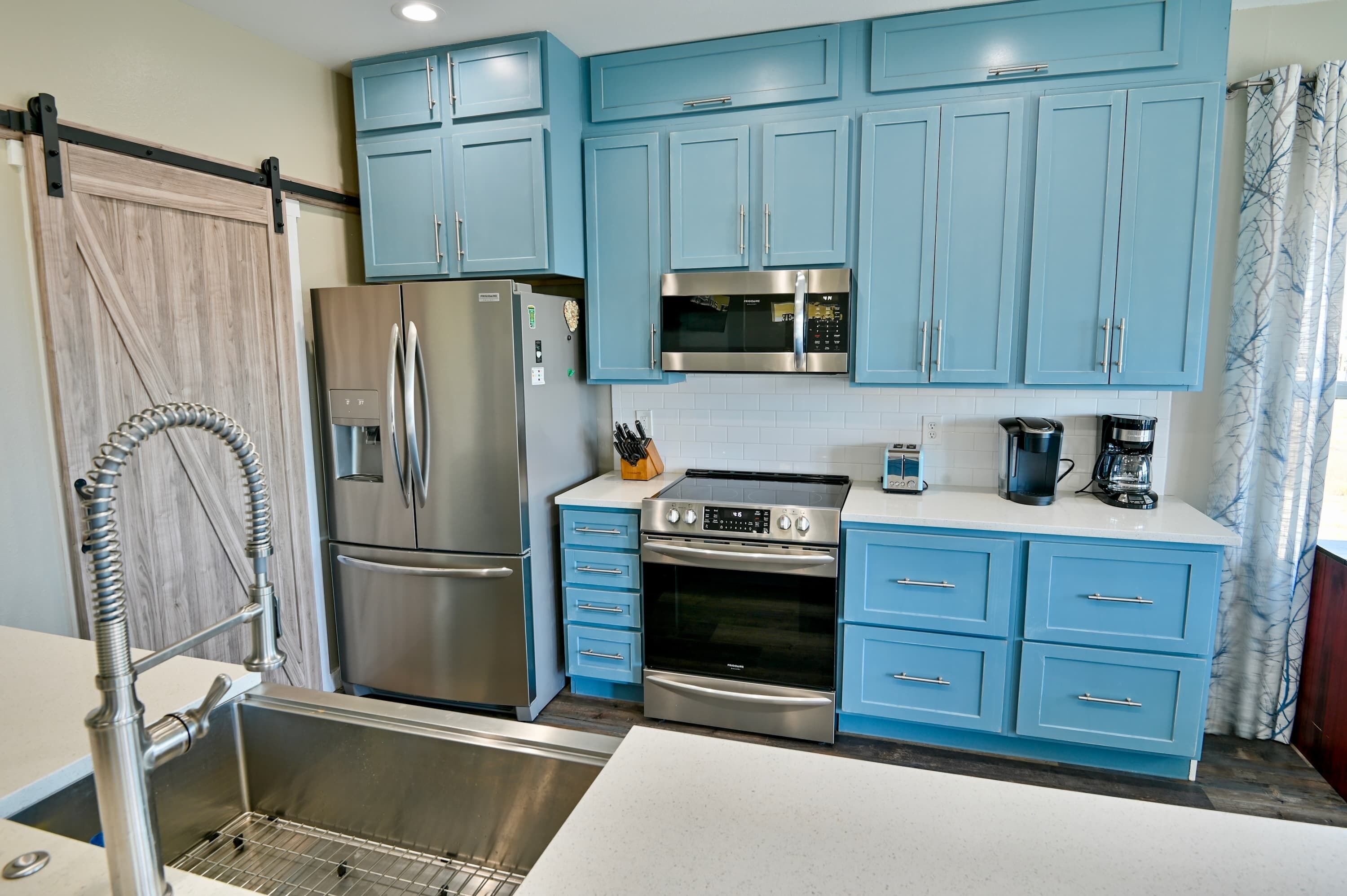A compact kitchen with blue cabinets, a stainless steel refrigerator, a microwave, an oven, and a coffee maker.