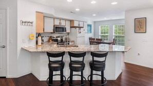 A modern kitchen with a granite countertop, stainless steel appliances, and three black bar stools. - Lake Hideaway Waterfront Condo w/ Resort Perks! (Kimberling City)