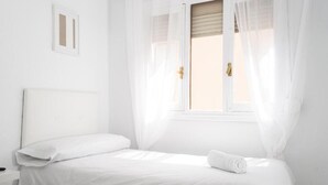 A white room with a bed, a nightstand, and a window with sheer curtains. - Hostal Alicia (Marbella)