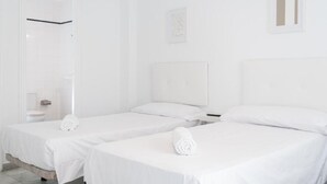 A hotel room with two single beds, a bathroom with a toilet and sink, and a white color scheme. - Hostal Alicia (Marbella)