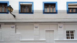 A building facade with white walls, blue window frames, and a central door with a grid pattern. - Hostal Alicia (Marbella)