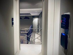 A hallway with a staircase, a door, and a wall-mounted control panel.