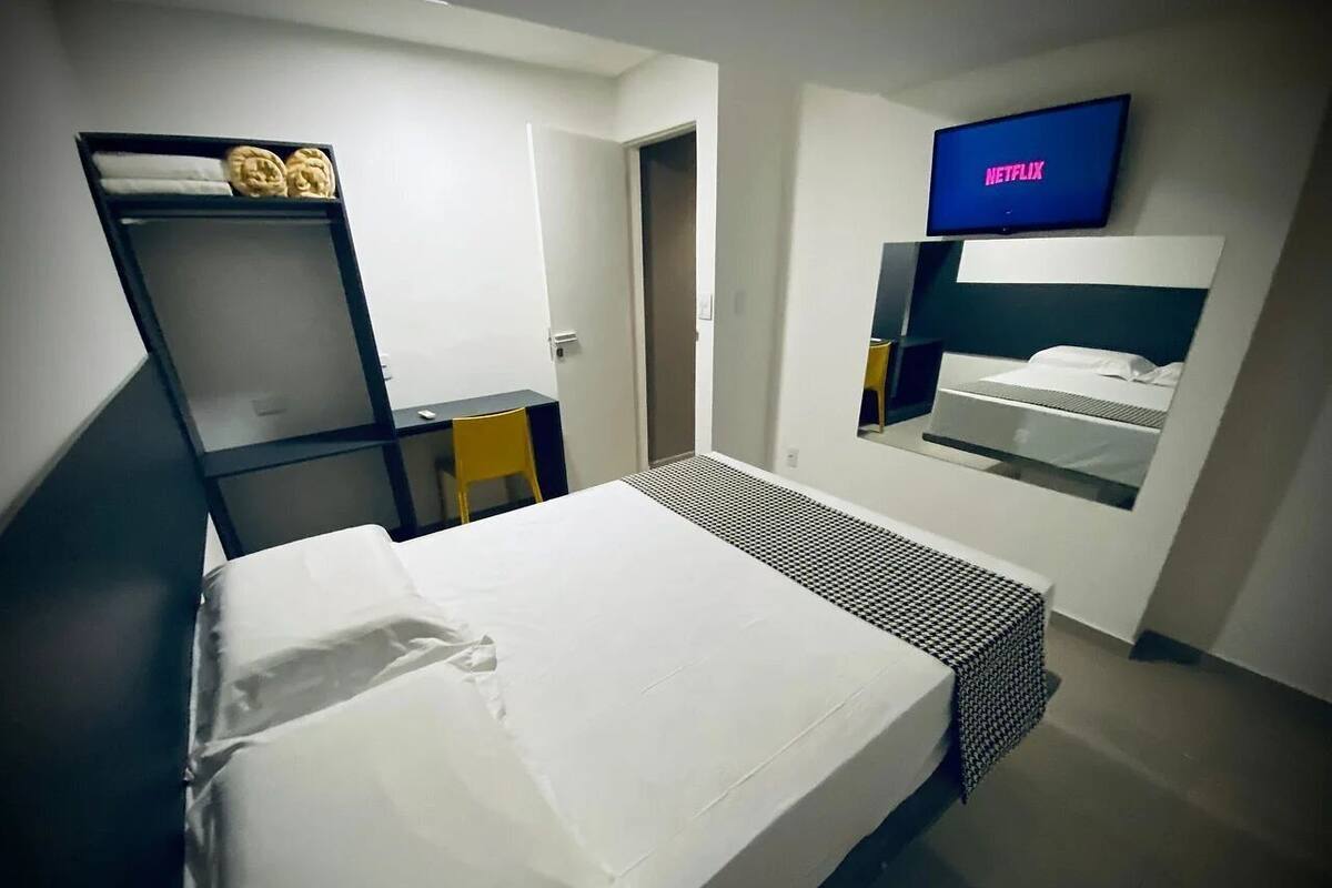 A hotel room with a bed, a TV mounted on the wall, a small desk, and a chair.
