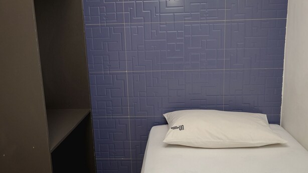 A small, single-bed room with a blue patterned wall and a white pillow. - Sun Smart Hotel (Recife)
