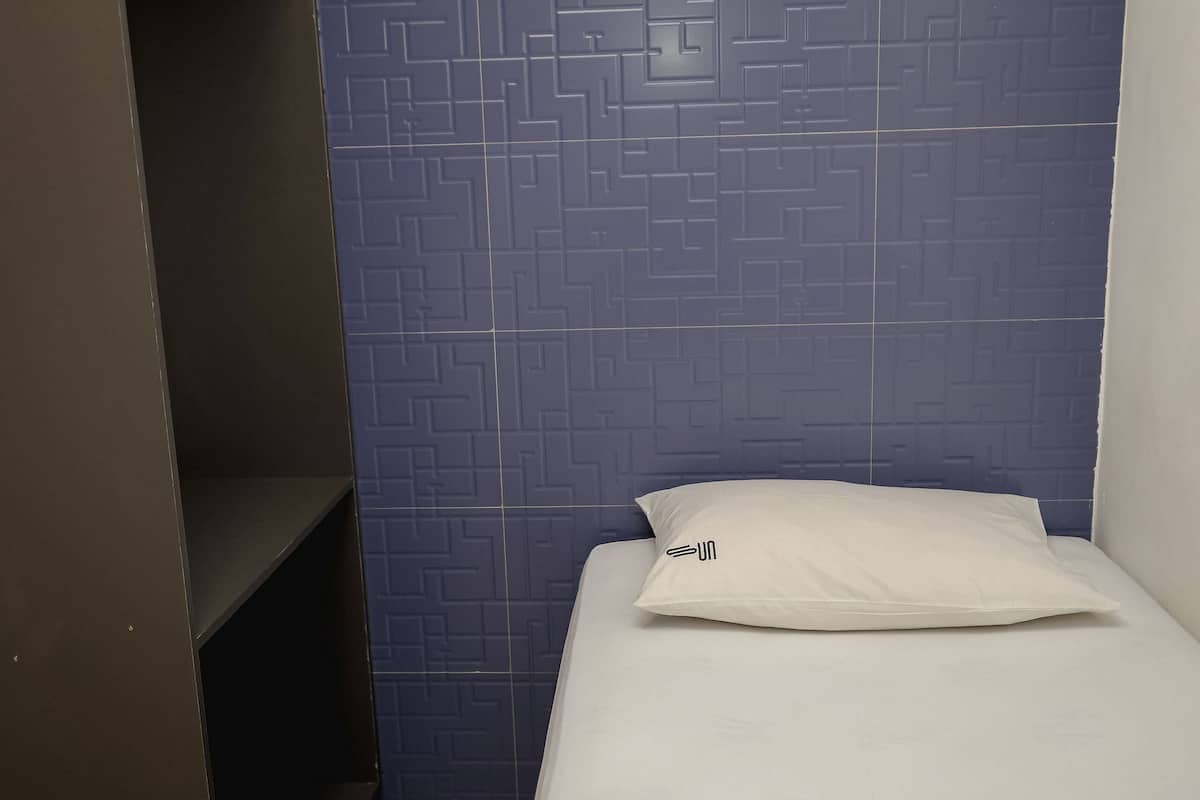 A small, single-bed room with a blue patterned wall and a white pillow.