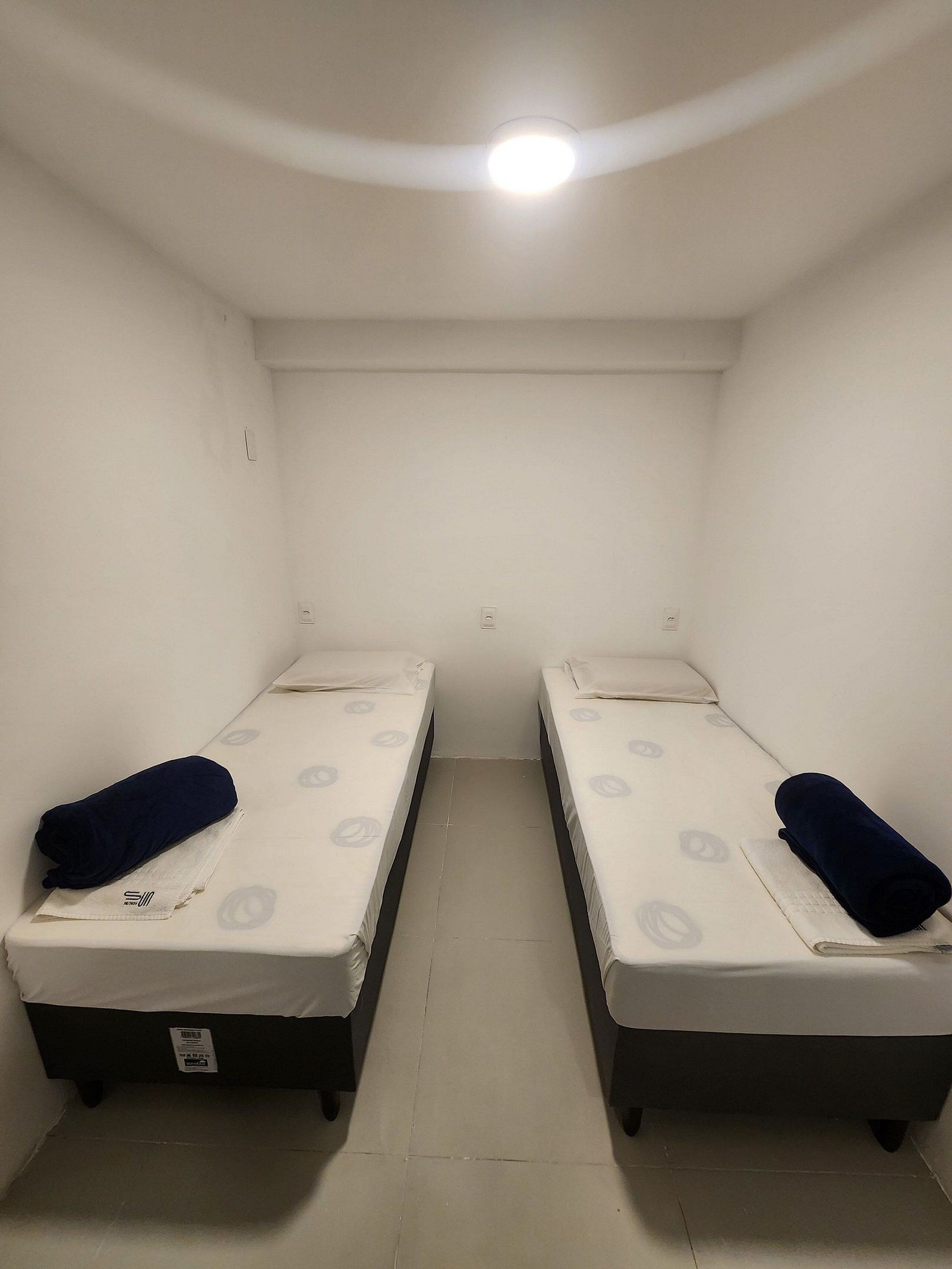 Una habitación pequeña y poco iluminada con dos camas individuales, cada una con una almohada y una manta.
