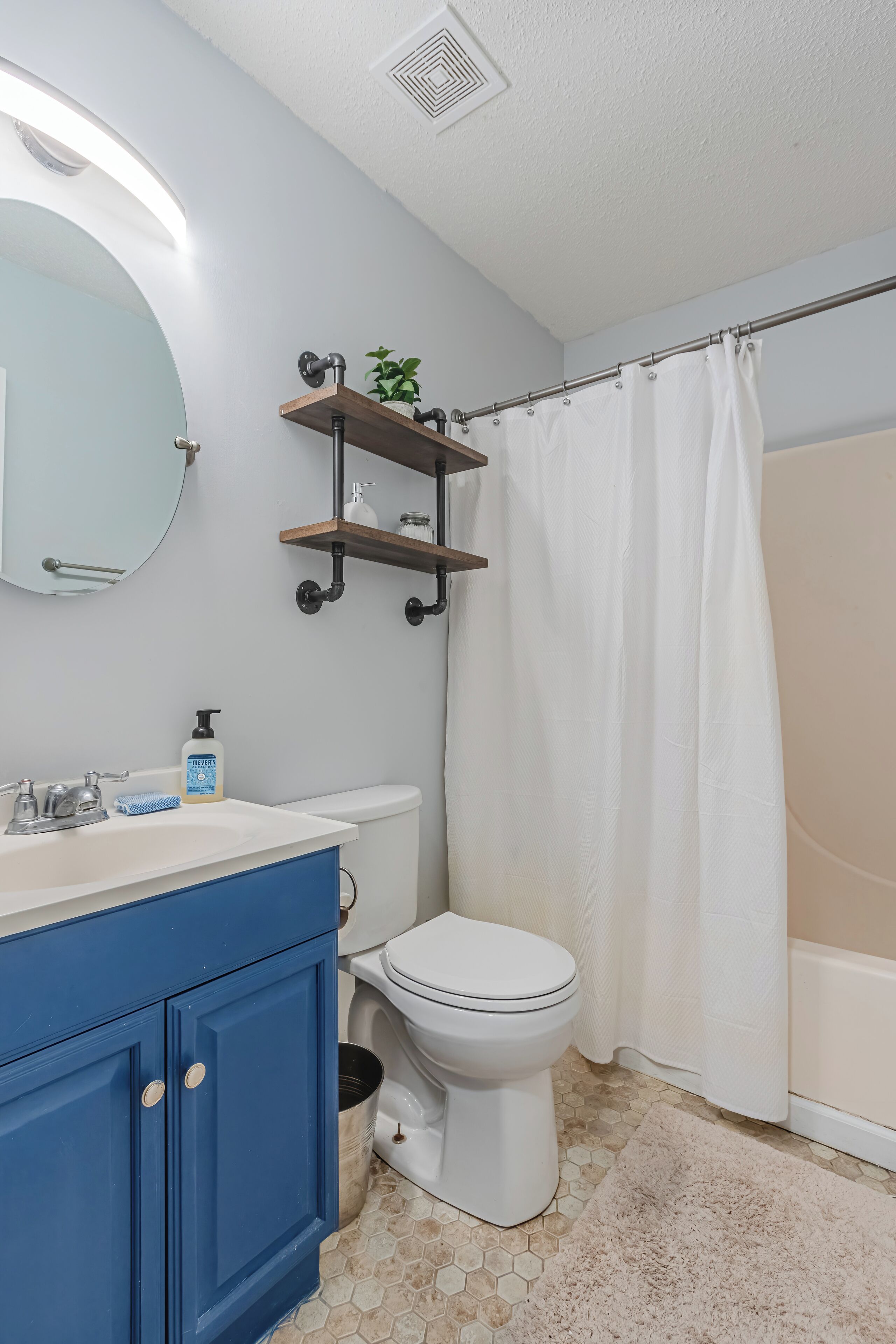 A bathroom with a white toilet, blue vanity, and a shower curtain.