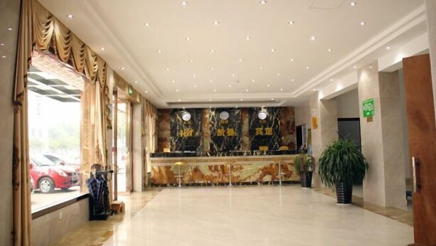 A hotel lobby with a marble reception desk, large windows with curtains, and a plant. - Hengdian Kaiman Hotel (Dongyang)